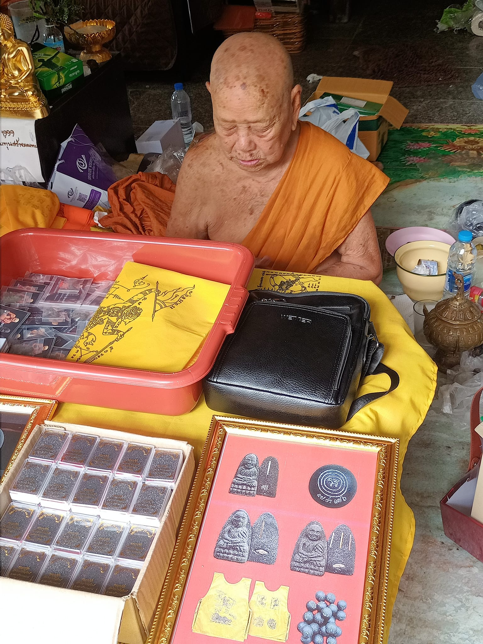 Luang Pu Thuad commemorative amulet 2023 displayed on table with Thai monk and framed amulet cases