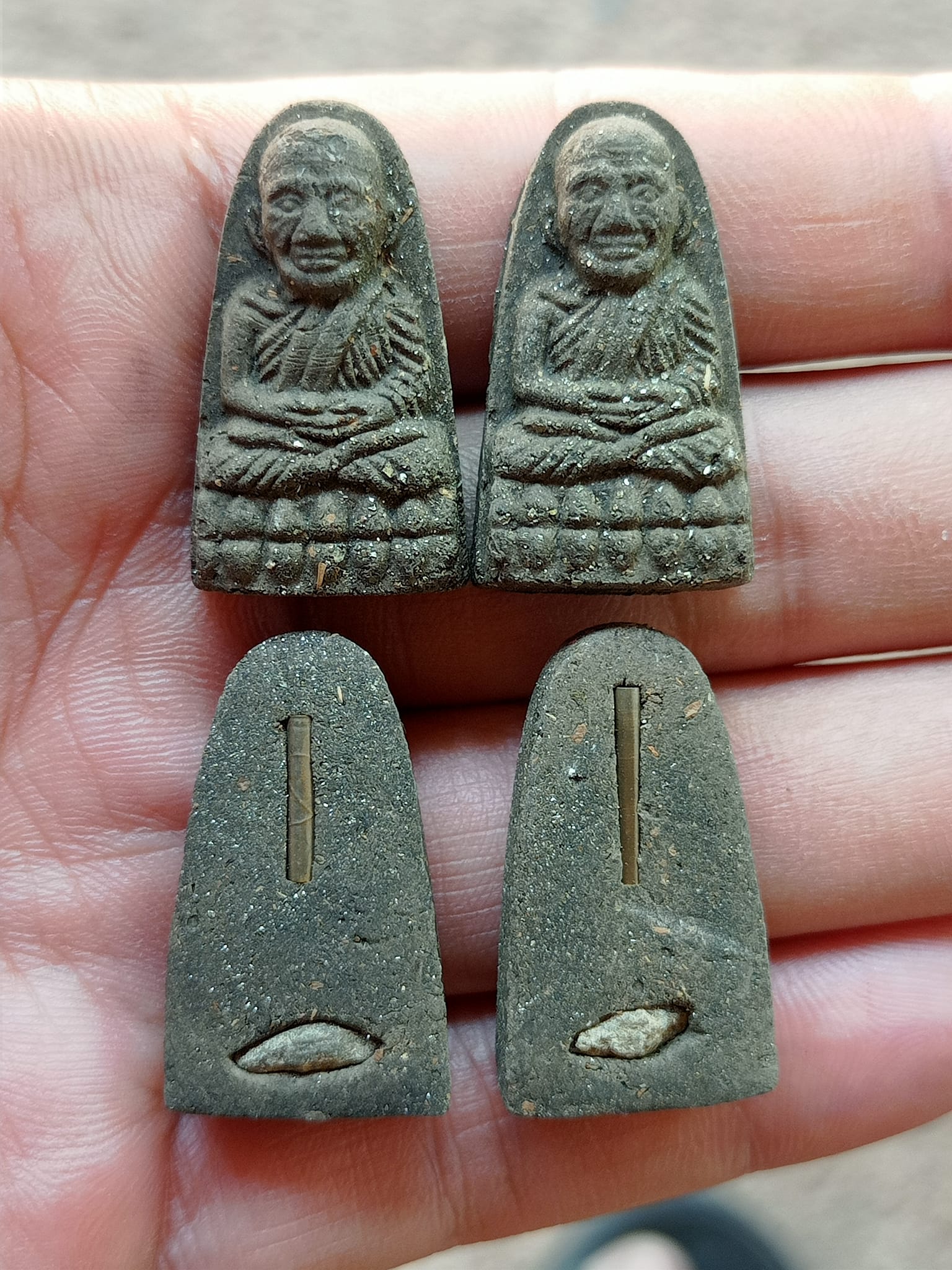 Hand holding four small Luang Pu Thuad commemorative amulet 2023 pieces showing front monk figures and backs