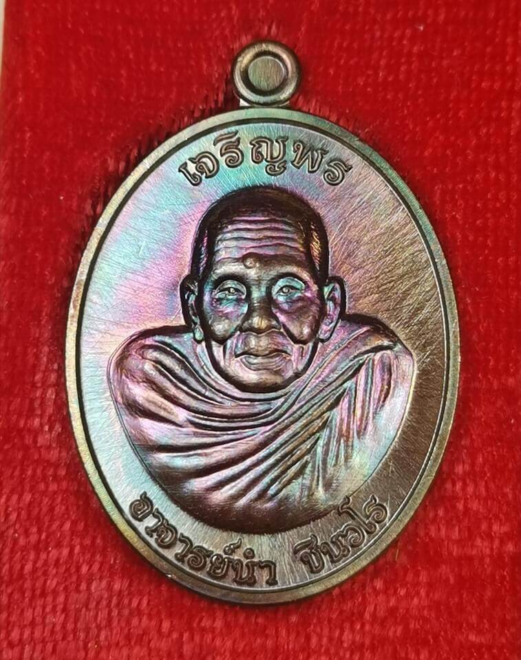 Iridescent metal pendant showing engraved elderly monk bust on red cloth background Phra Charoen Phon Hoom Kloom amulet