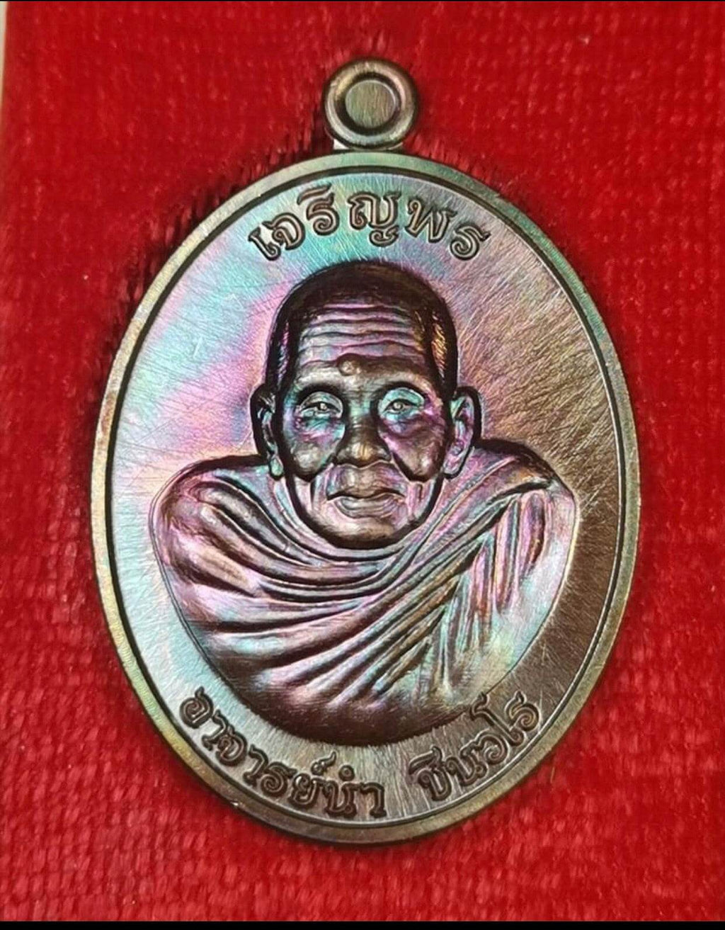 Phra Charoen Phon Hoom Kloom amulet metal oval medallion with elderly monk portrait and Thai script on red cloth