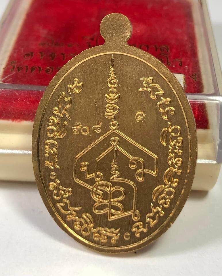 Gold oval Phra Charoen Phon Hoom Kloom amulet medallion with Thai yantra and script displayed on red velvet box
