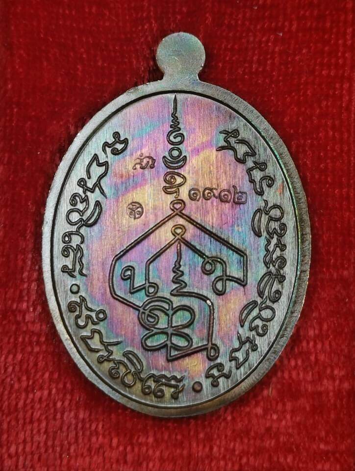 Iridescent oval metal amulet pendant with Thai yantra engravings on red cloth Phra Charoen Phon Hoom Kloom amulet