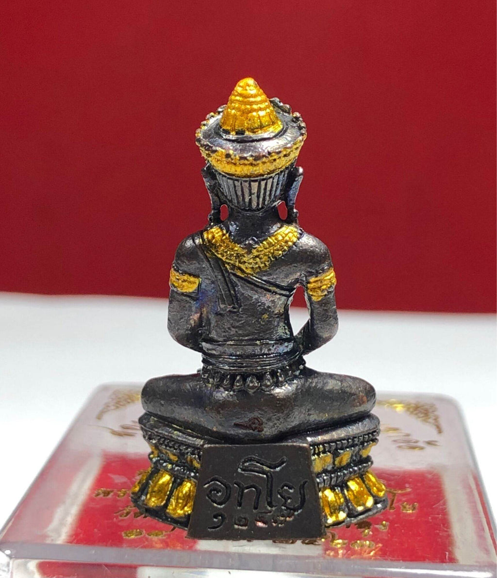 Phra Kring Arkom Amulet seated metal figure with gold highlights on ornate pedestal against red background