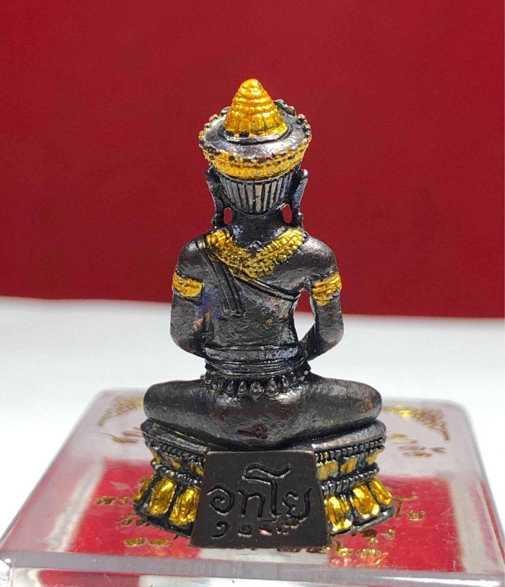 Phra Kring Arkom Amulet seated metal figure with gold highlights on ornate pedestal against red background