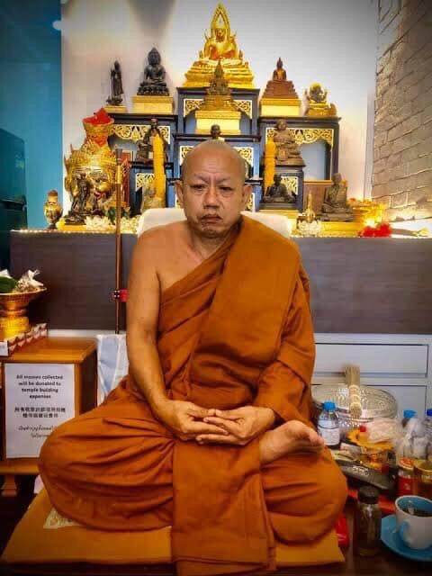 Buddhist monk seated by shrine with Phra Kring Arkom Amulet display and altar for blessing amulets