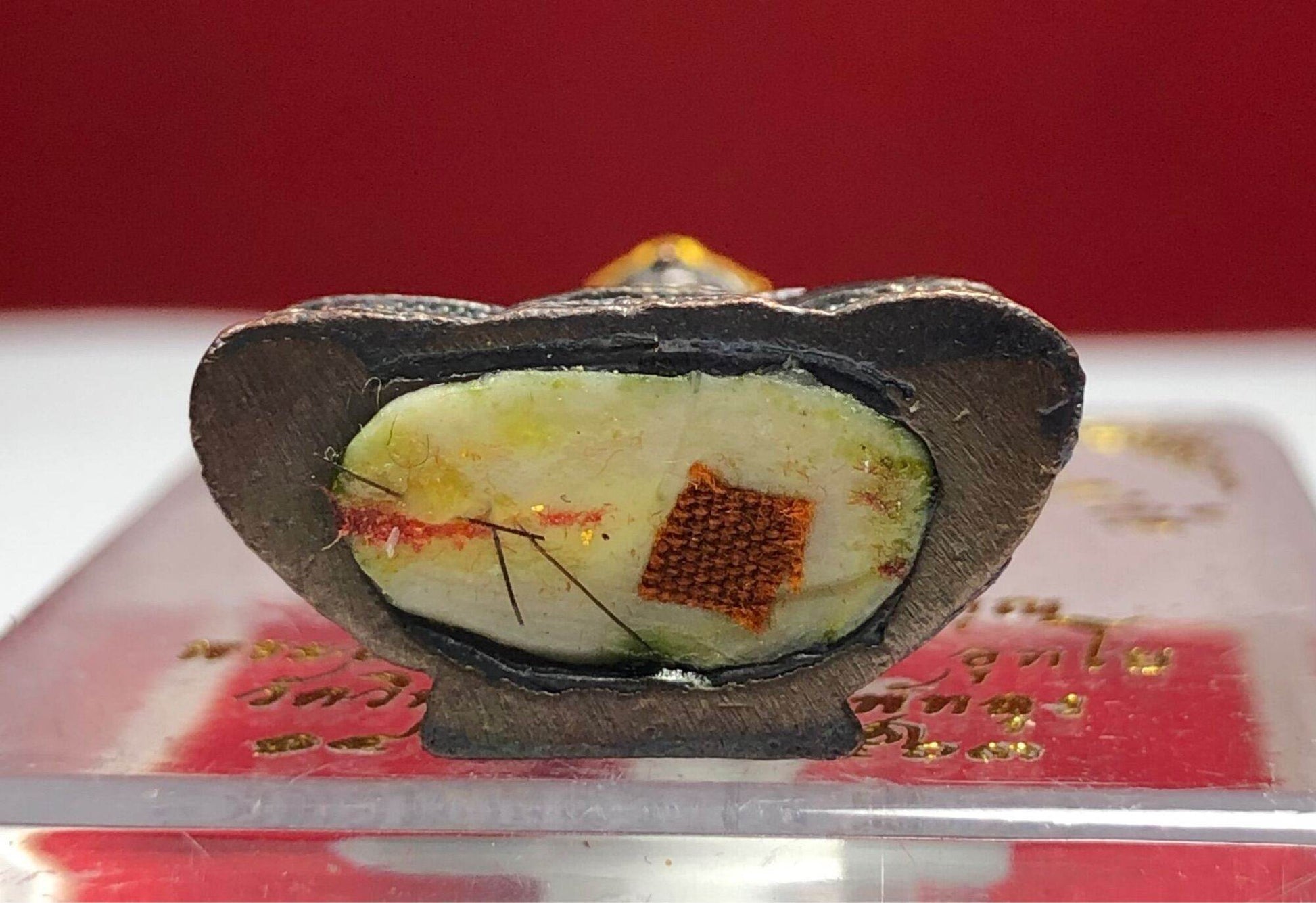 Close up cross section of Phra Kring Arkom Amulet pendant showing metal casing and inner relic cloth