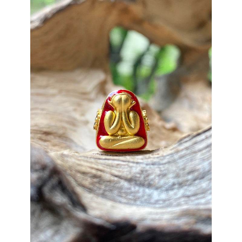 Phra Pidta amulet gold enamel seated figure covering eyes small Thai talisman on rustic wood background