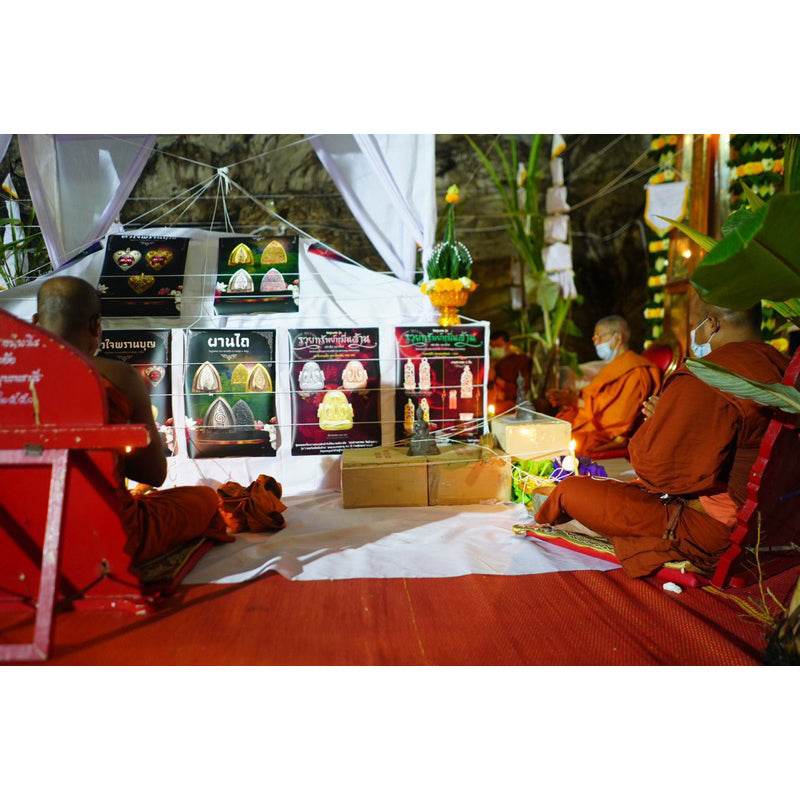 Phra Pidta amulet gold enamel displayed at Thai Blessing Co shrine with monks performing blessing ritual