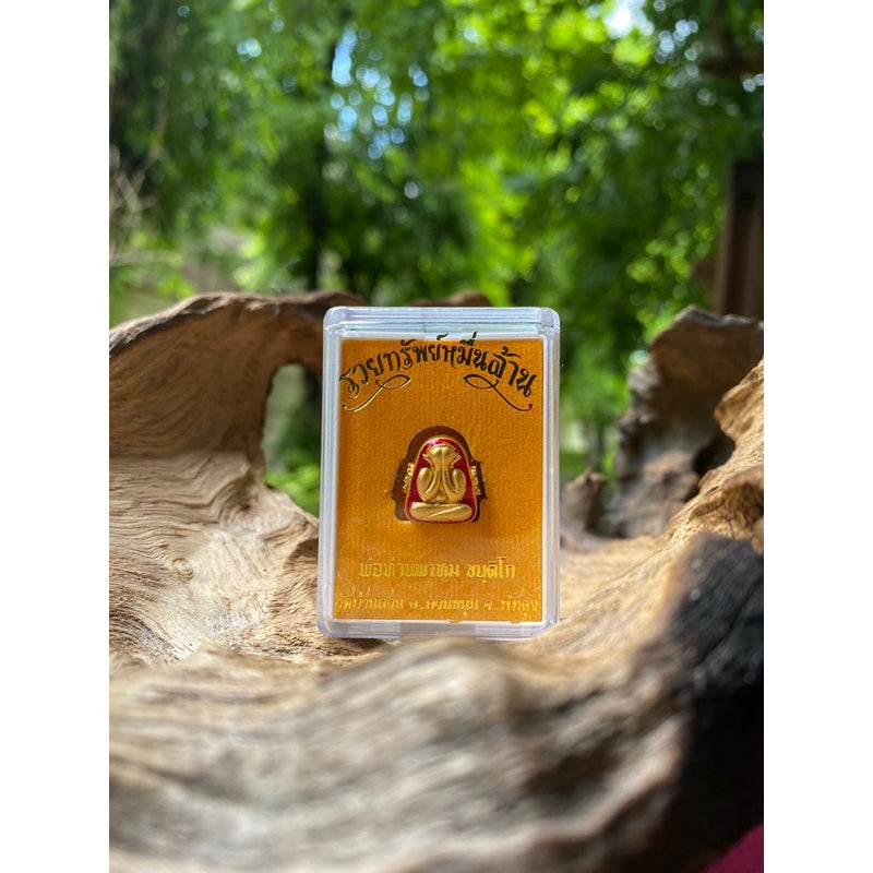 Phra Pidta amulet gold enamel in clear plastic case on natural wood for Thai blessing decor