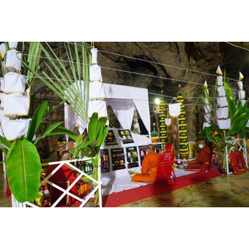Thai blessing ceremony with monks in a cave shrine displaying Phra Pidta amulet gold enamel on altar