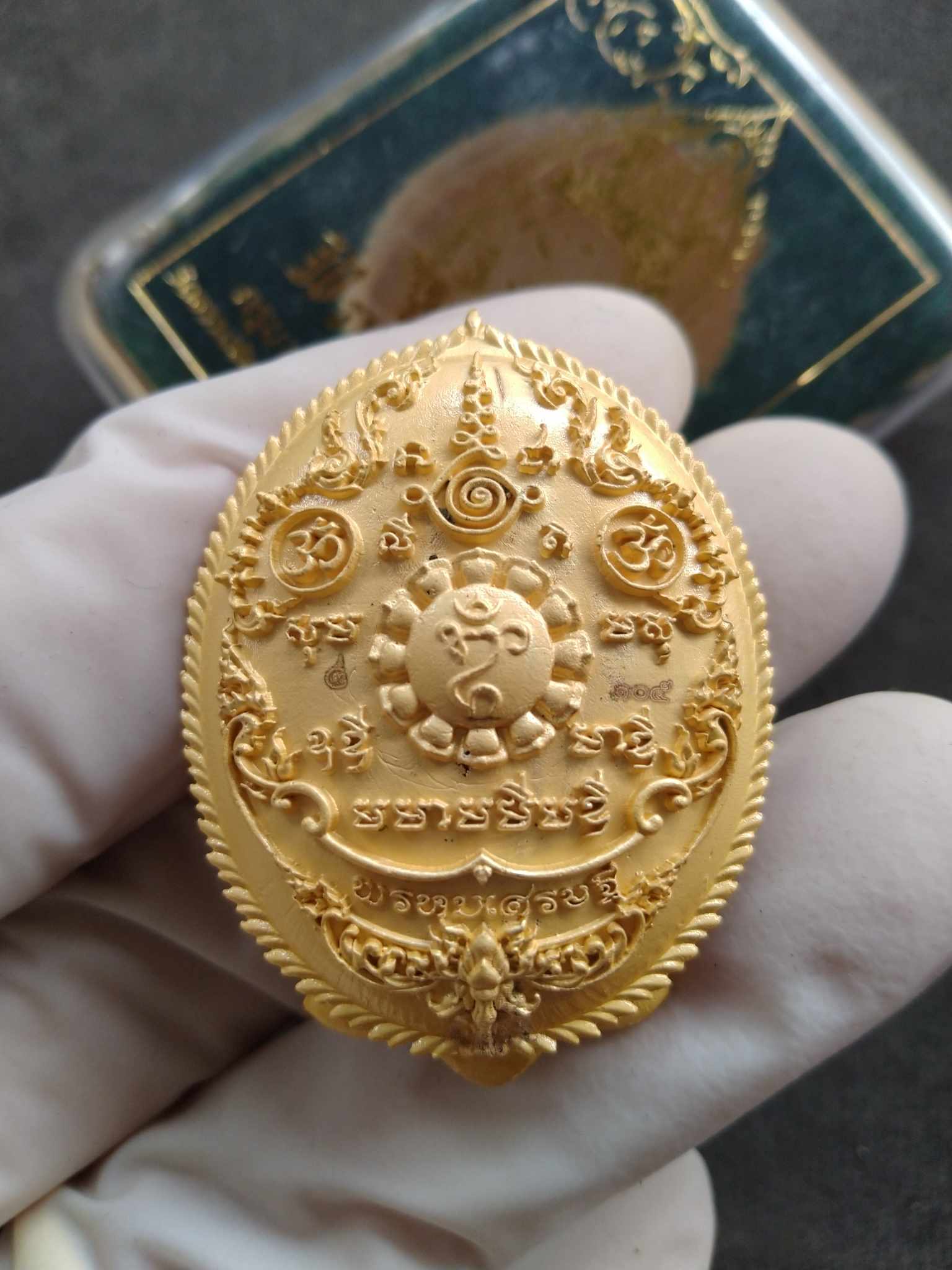 Phrom Setthi blessed coin amulet gold oval Thai pendant with sacred inscriptions held by gloved hand