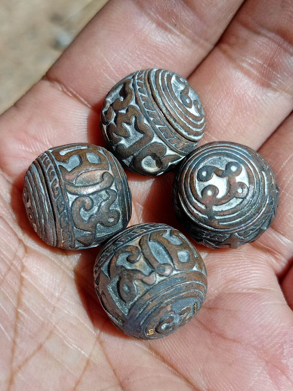 Hand holding four engraved round sacred bullet amulet Thailand beads with aged patina