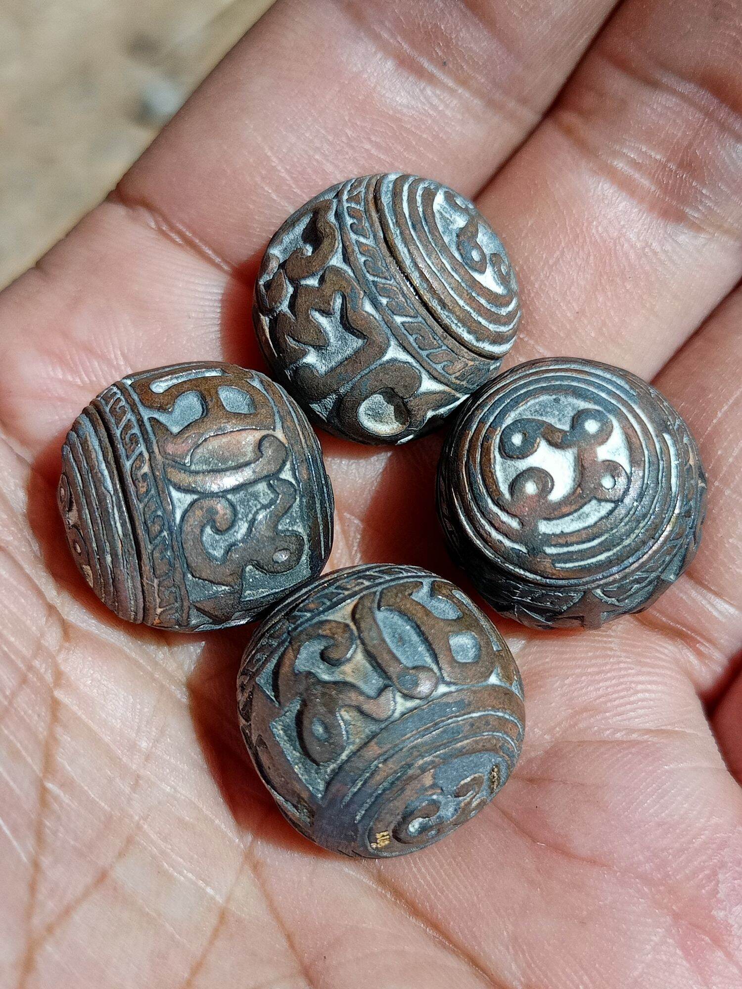 Hand holding four engraved round sacred bullet amulet Thailand beads with aged patina