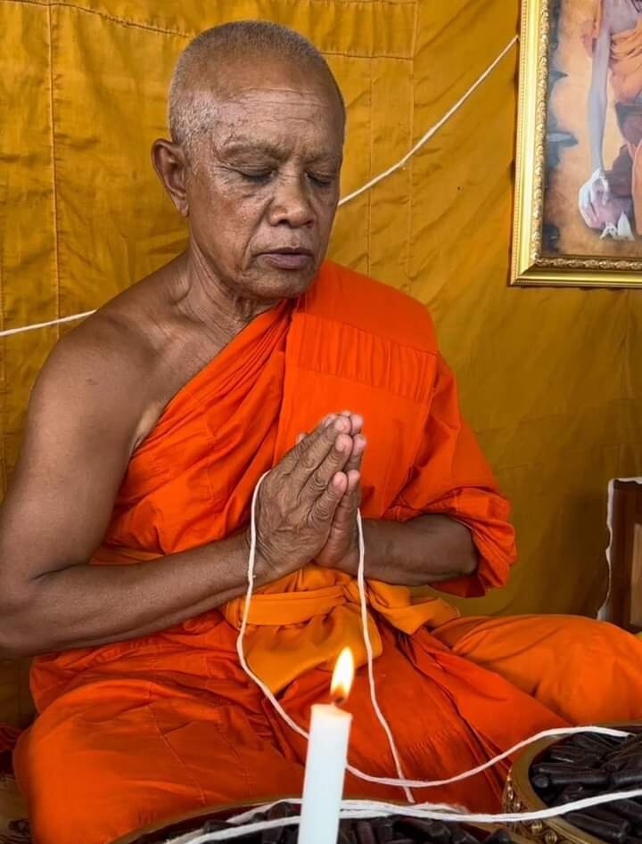 Thai monk in orange robes blessing a pendant with candle and white string during ceremony for sacred bullet amulet Thailand
