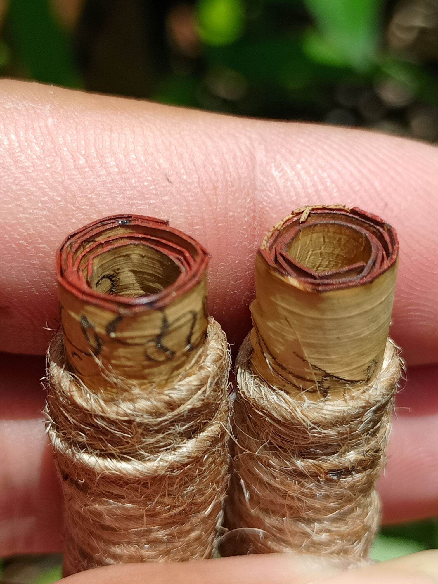 Close up of two Thai amulet scroll pendants wrapped in natural twine sacred protection charm for fortune