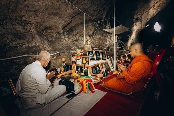 Sangkajai Buddha amulet for wealth displayed on cave altar with monk and offerings during blessing ritual