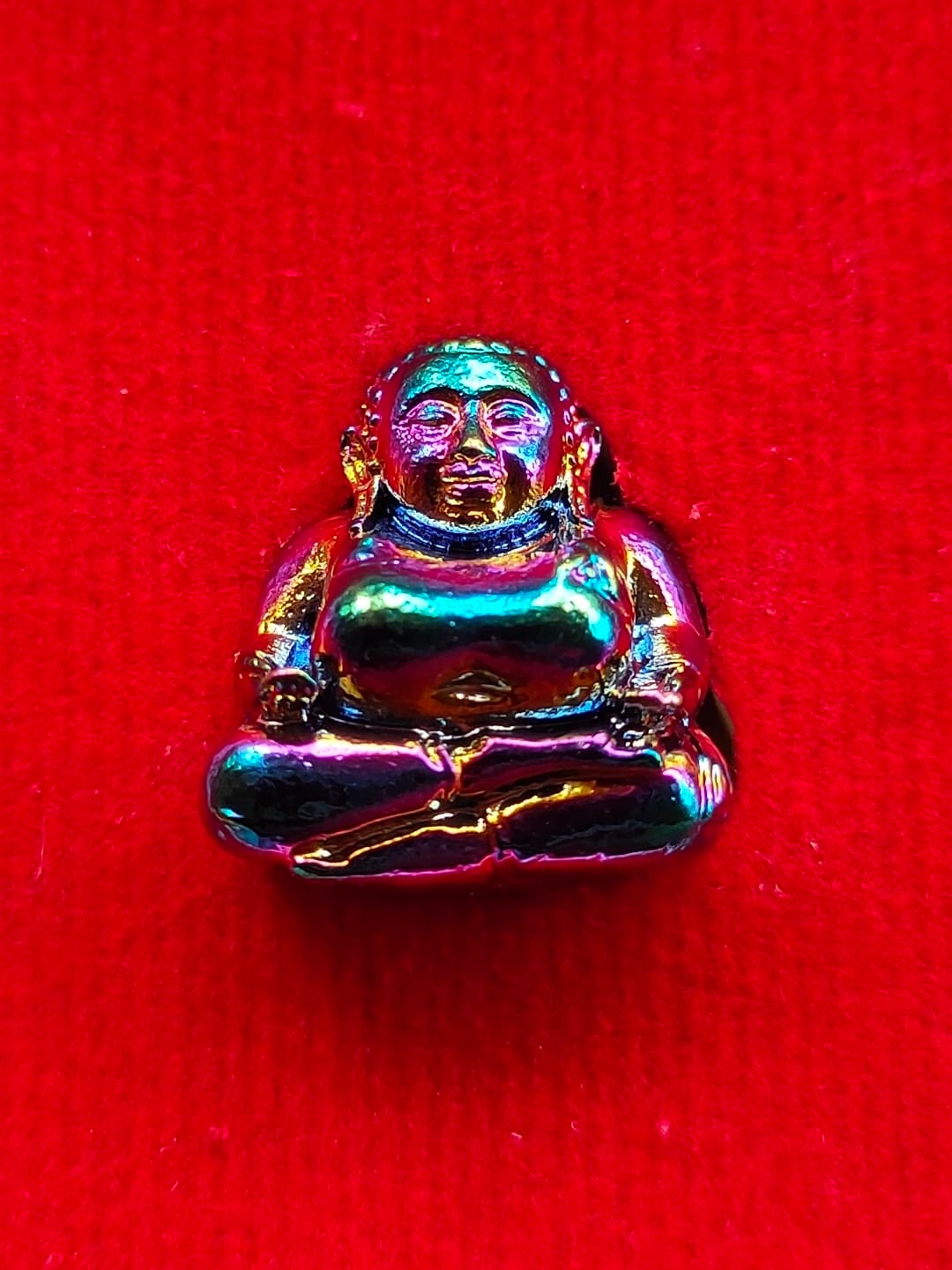 Sangkajai Buddha amulet for wealth iridescent metal statue on red fabric background by Thai Blessing Co