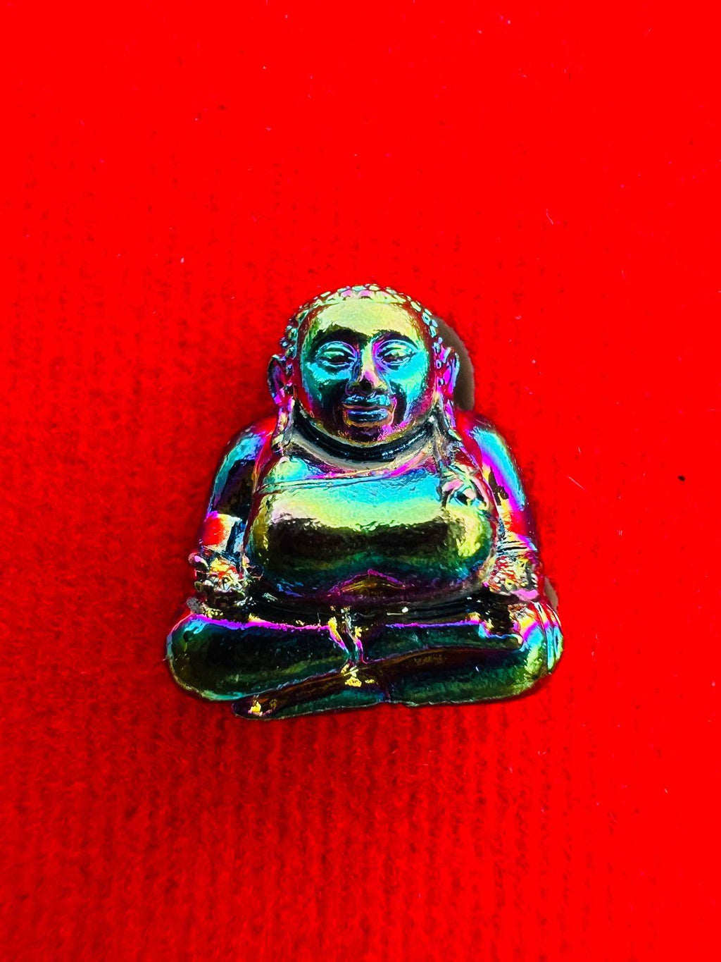 Iridescent metal Sangkajai Buddha amulet for wealth seated on red fabric pocket talisman by Thai Blessing Co