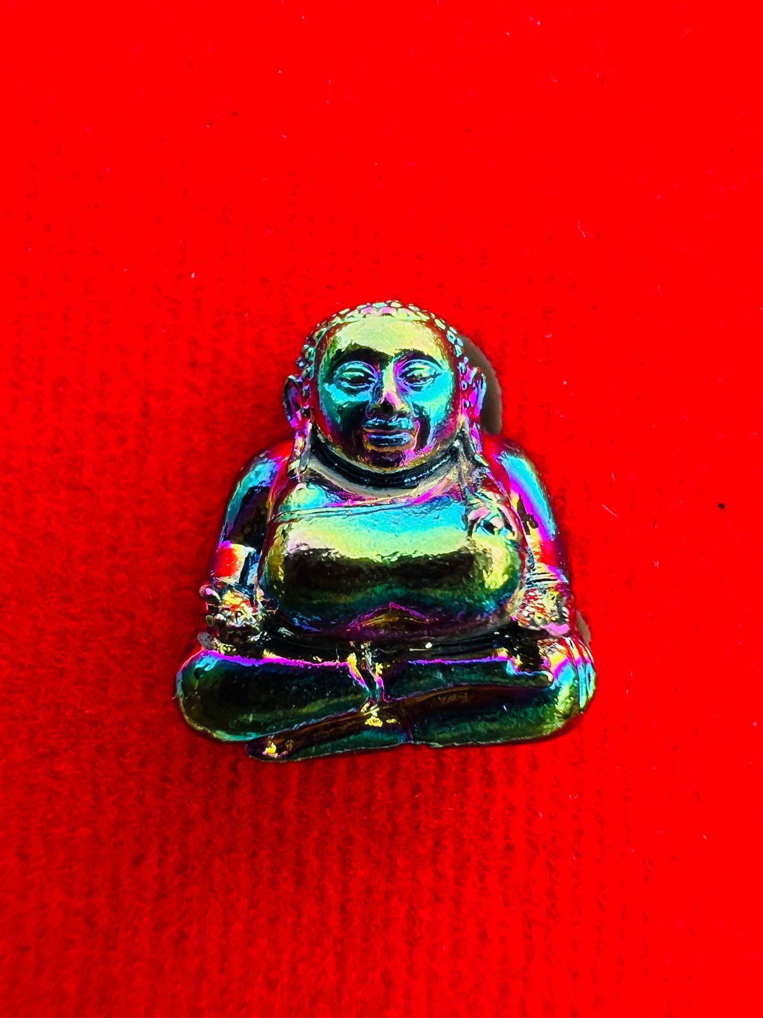 Iridescent metal Sangkajai Buddha amulet for wealth seated on red fabric pocket talisman by Thai Blessing Co