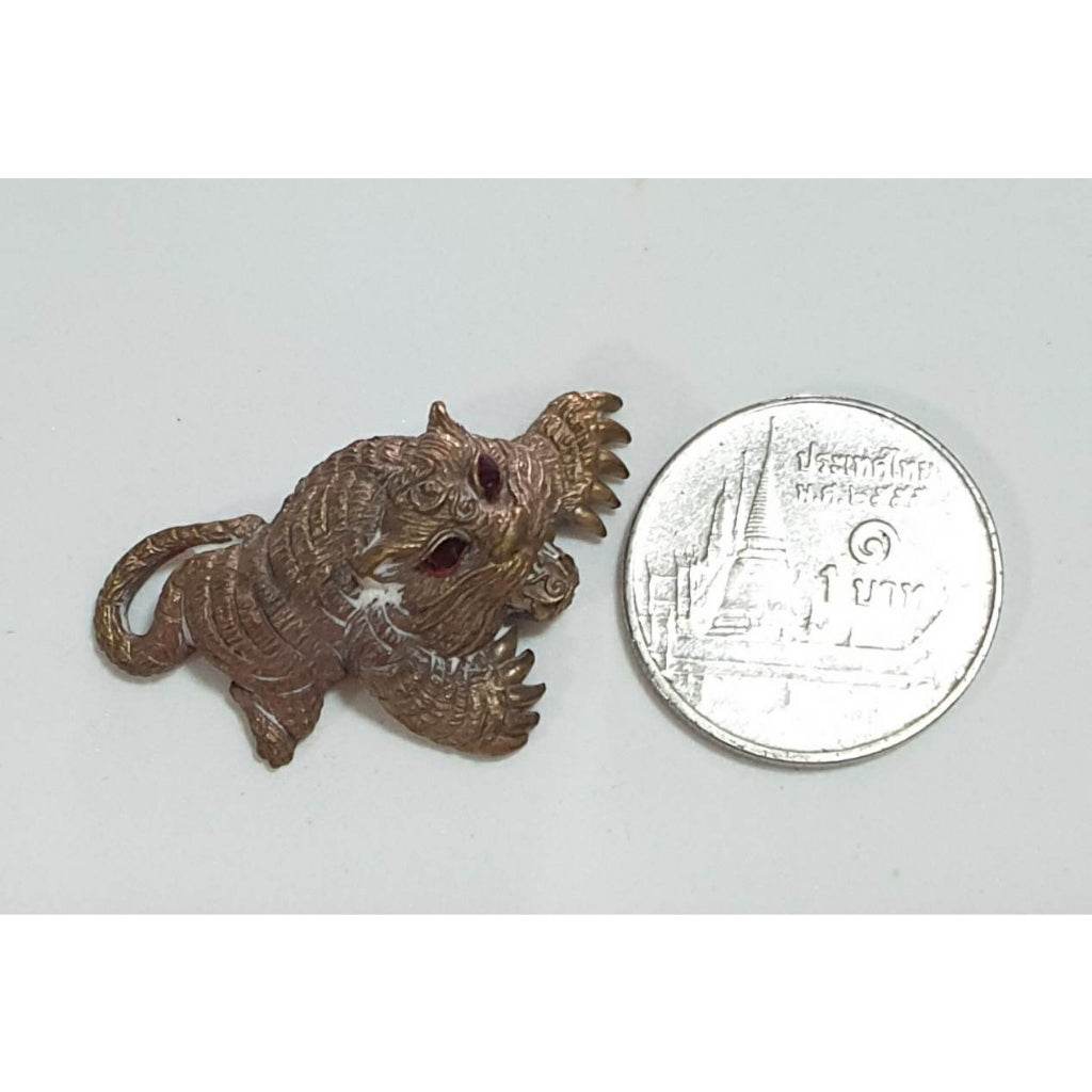 Bronze tiger amulet with red stone eyes beside Thai coin for scale small talisman Thai amulets for wealth