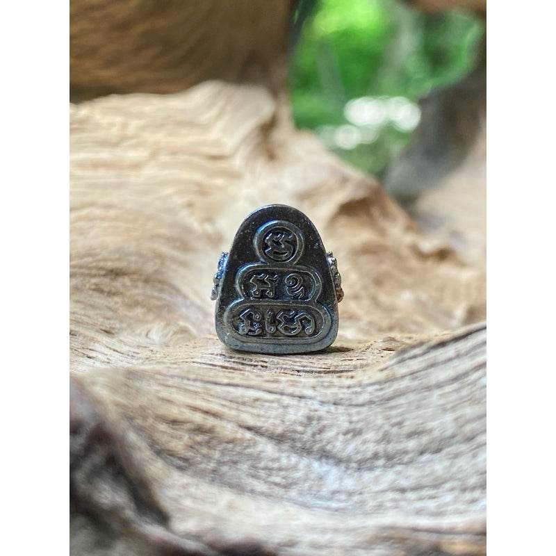 Close up metal amulet with Thai script and stacked motifs on driftwood background Thai billionaire wealth amulet
