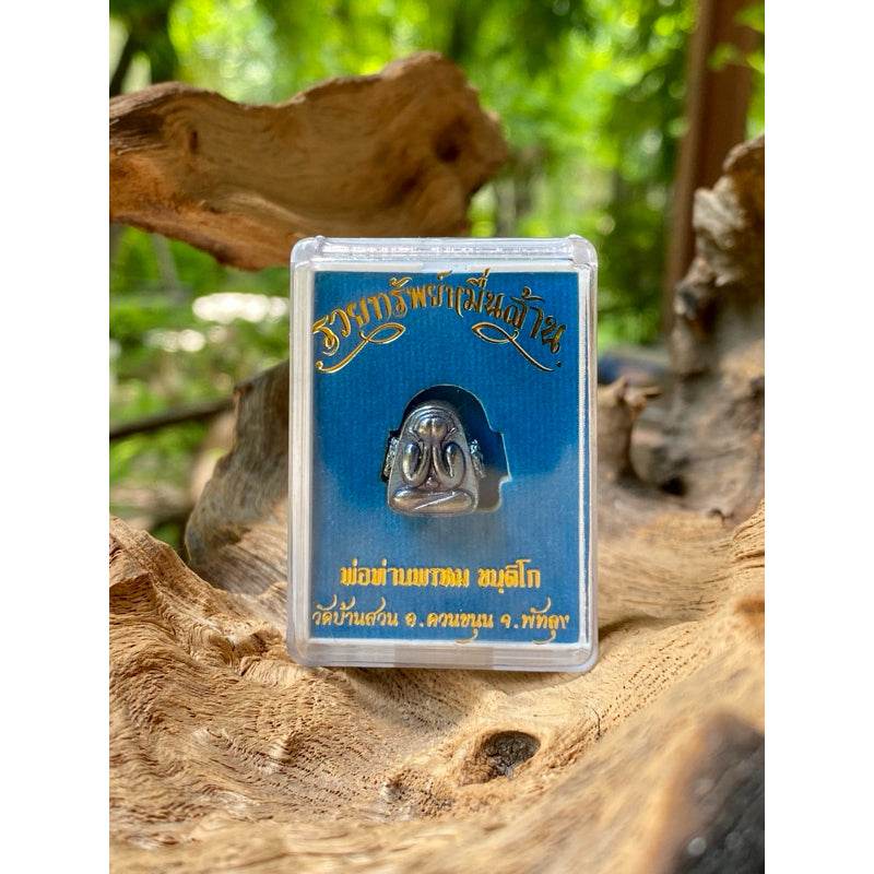 Thai billionaire wealth amulet silver talisman in clear plastic display case on natural wood backdrop