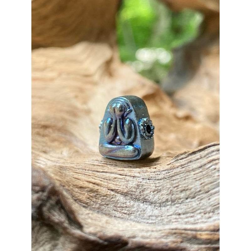 Iridescent Phra Pidta meditation amulet with black side stone on natural wood display Thai billionaire wealth amulet