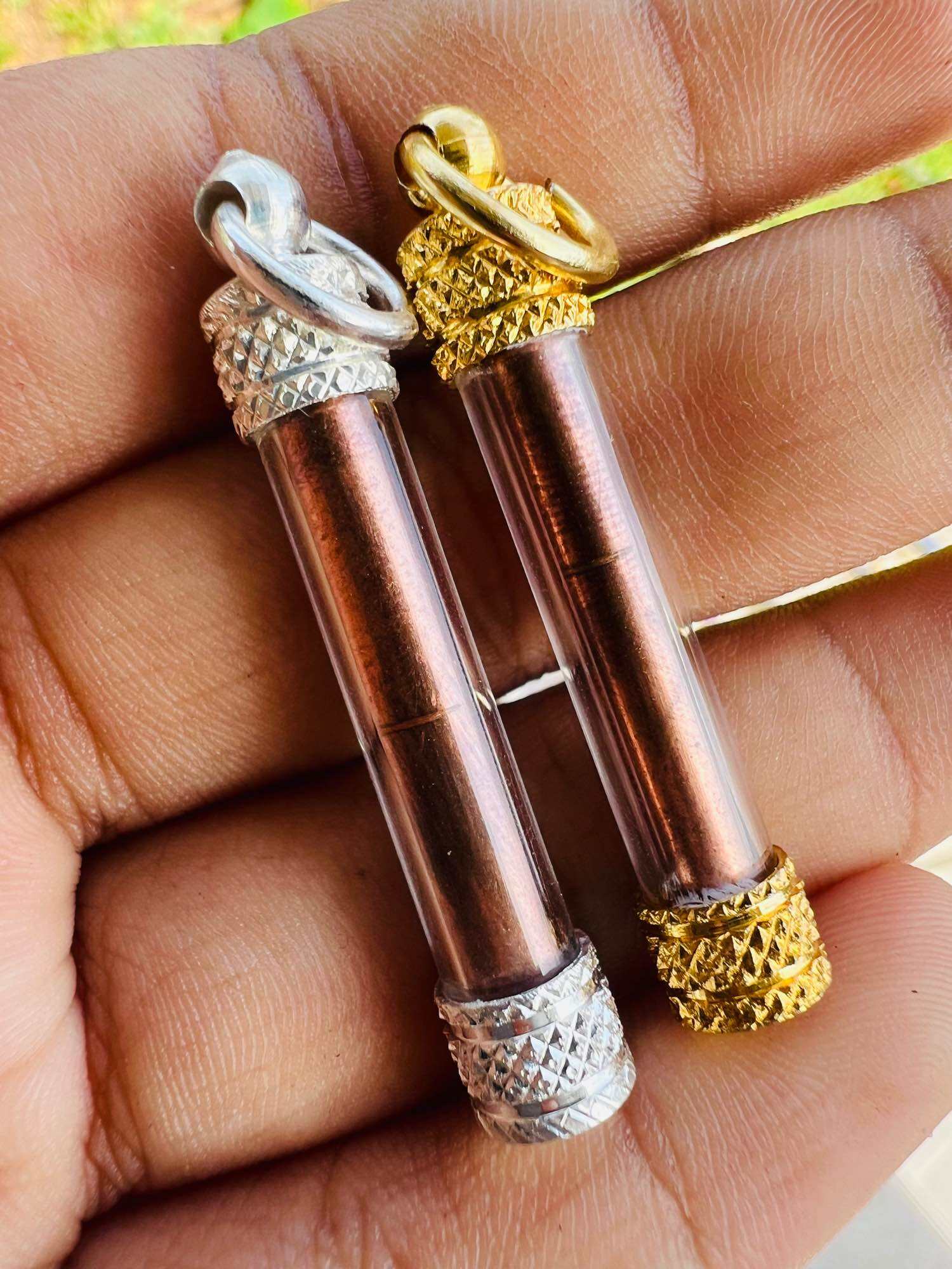 Hand holding two Thai elephant takrud amulet copper scroll tubes with gold and silver ornate end caps