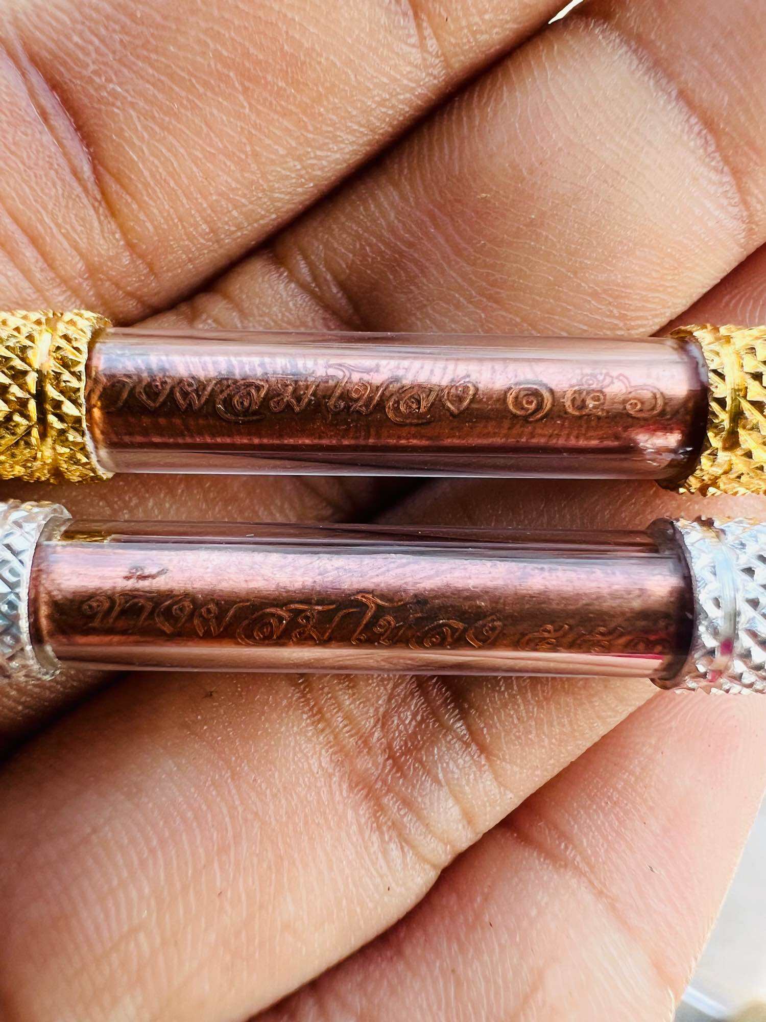 Close up of two copper scroll takruds in clear tubes with gold and silver end caps held in hand Thai elephant takrud amulet