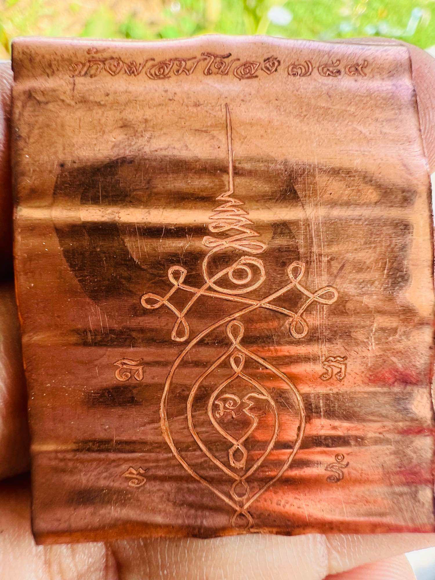 Handheld copper Thai elephant takrud amulet sheet with engraved sacred yantra and Thai script