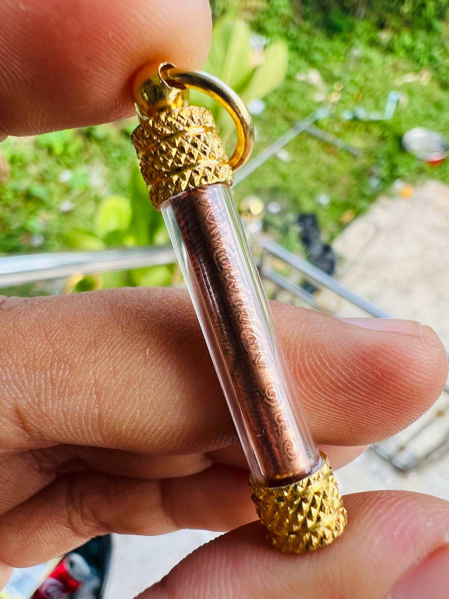 Handheld Thai elephant takrud amulet in glass tube with copper scroll and gold caps on a finger