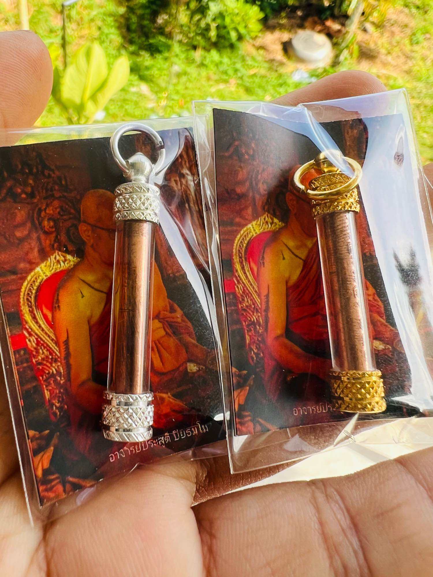 Thai elephant takrud amulet pair with copper tubes and silver and gold caps on monk backing cards held in hand