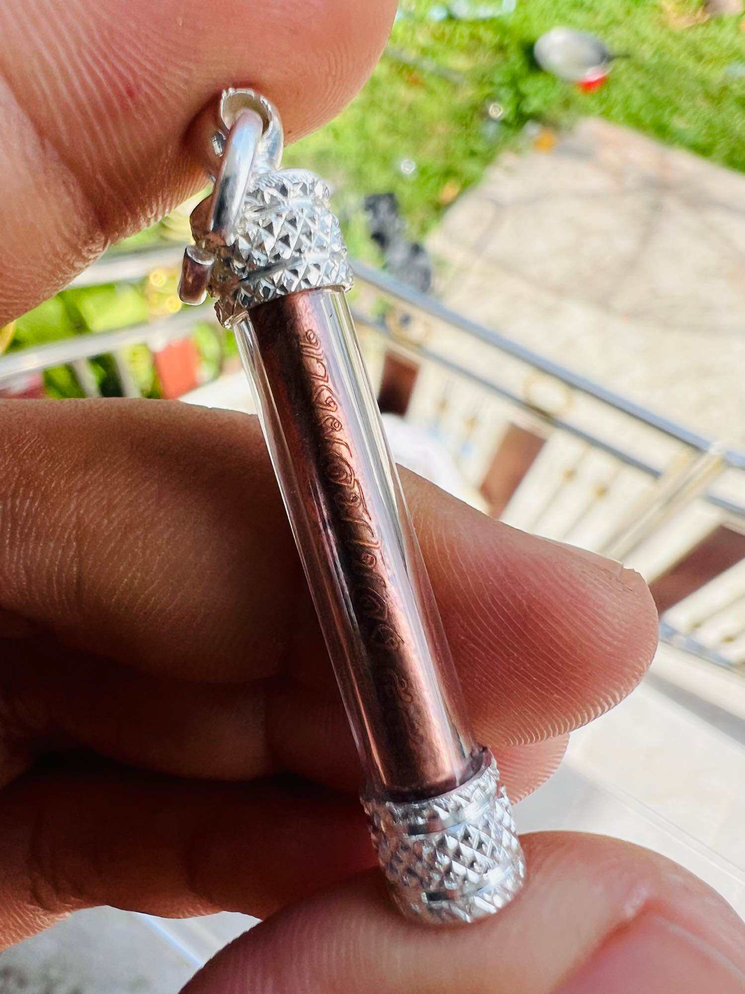 Thai elephant takrud amulet copper scroll in clear glass tube with silver textured caps held between fingers