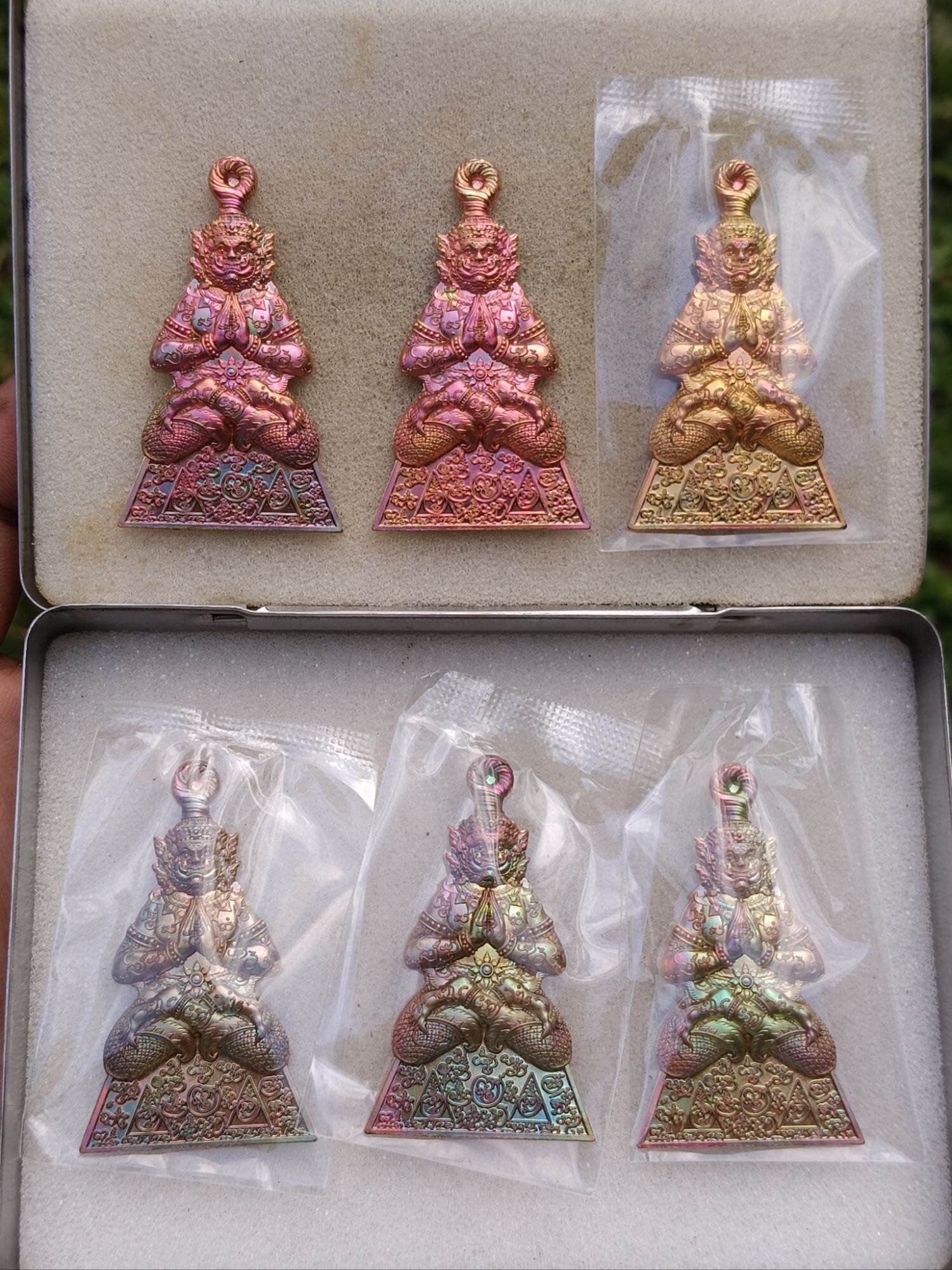 Thai guardian spirit protection charm pendant set in foam box showing six iridescent metal amulets by Thai Blessing Co