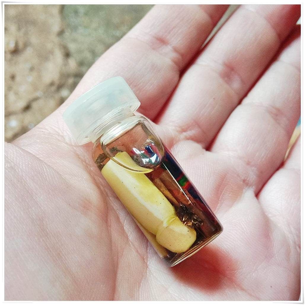 Small glass vial in palm with carved ivory figure colored threads and oil Thai love and fortune talisman