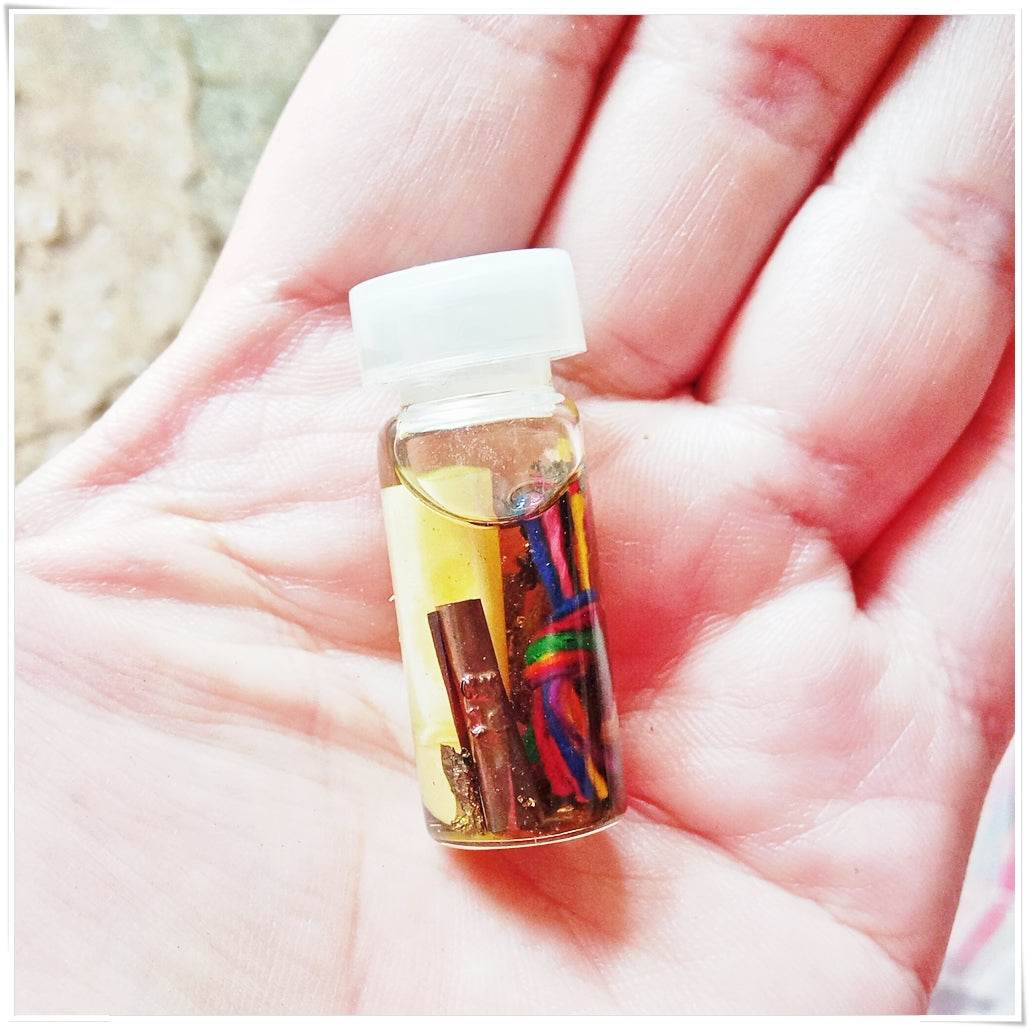 Small glass vial Thai love and fortune talisman with colorful threads and metal charm in hand