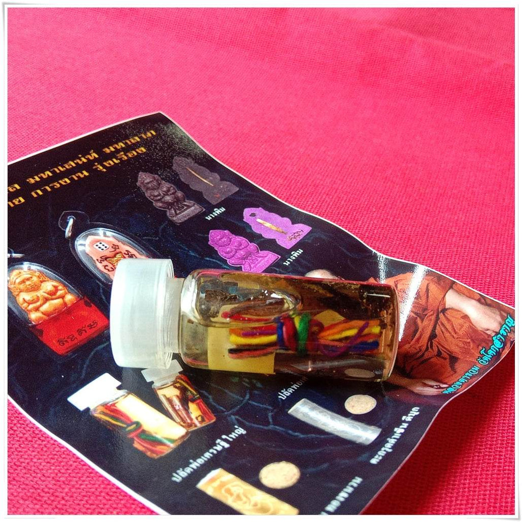 Small glass vial amulet with colorful threads and herbs on brochure over pink cloth Thai love and fortune talisman