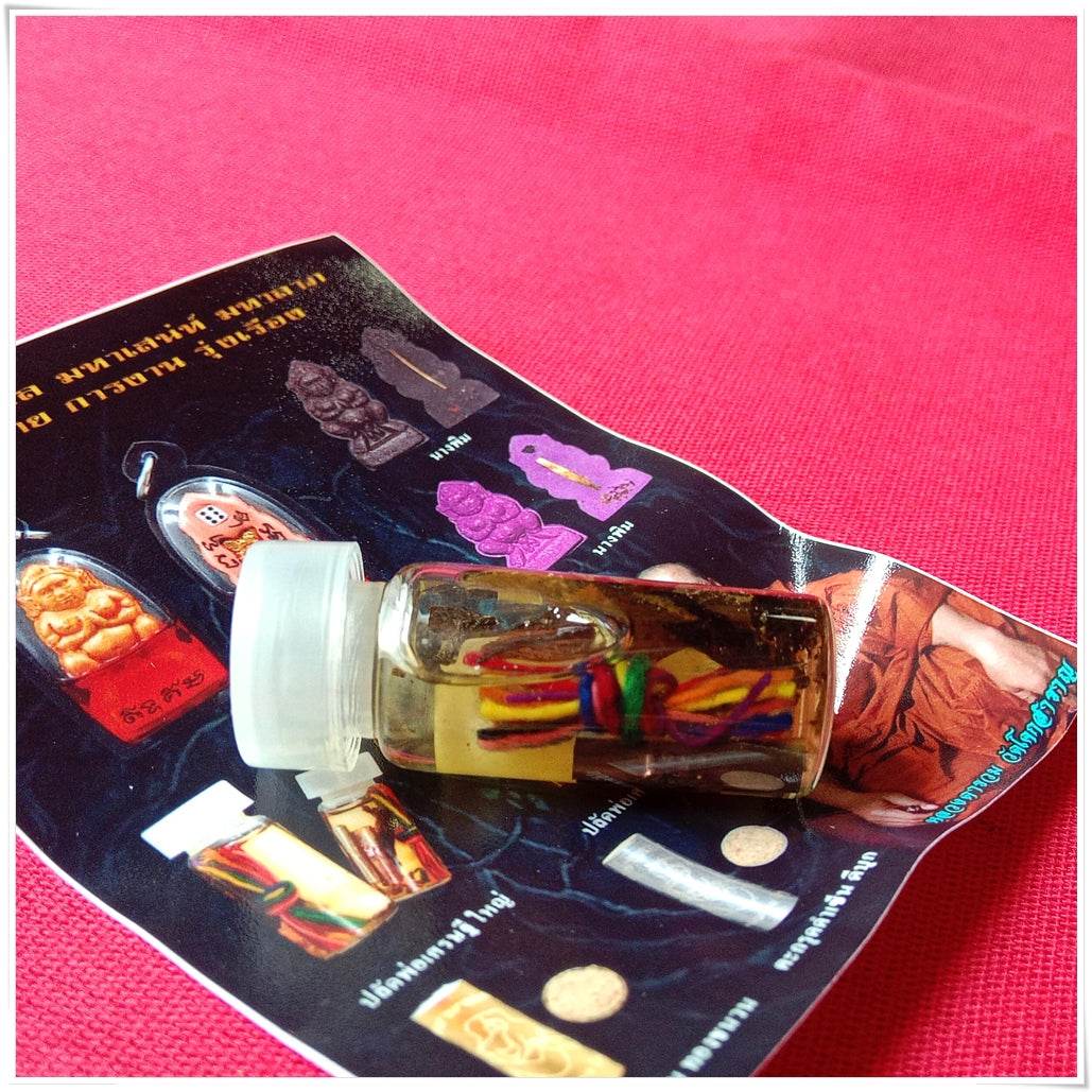 Small glass vial amulet with colorful threads and herbs on brochure over pink cloth Thai love and fortune talisman