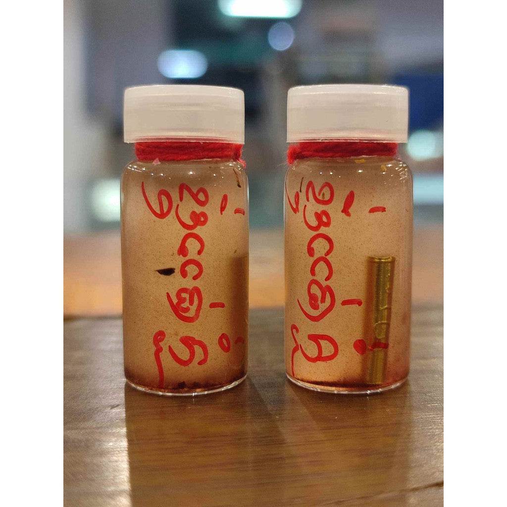 Two small glass amulet vials with white caps and red Thai script powder and gold pellet inside Thai love attraction oil