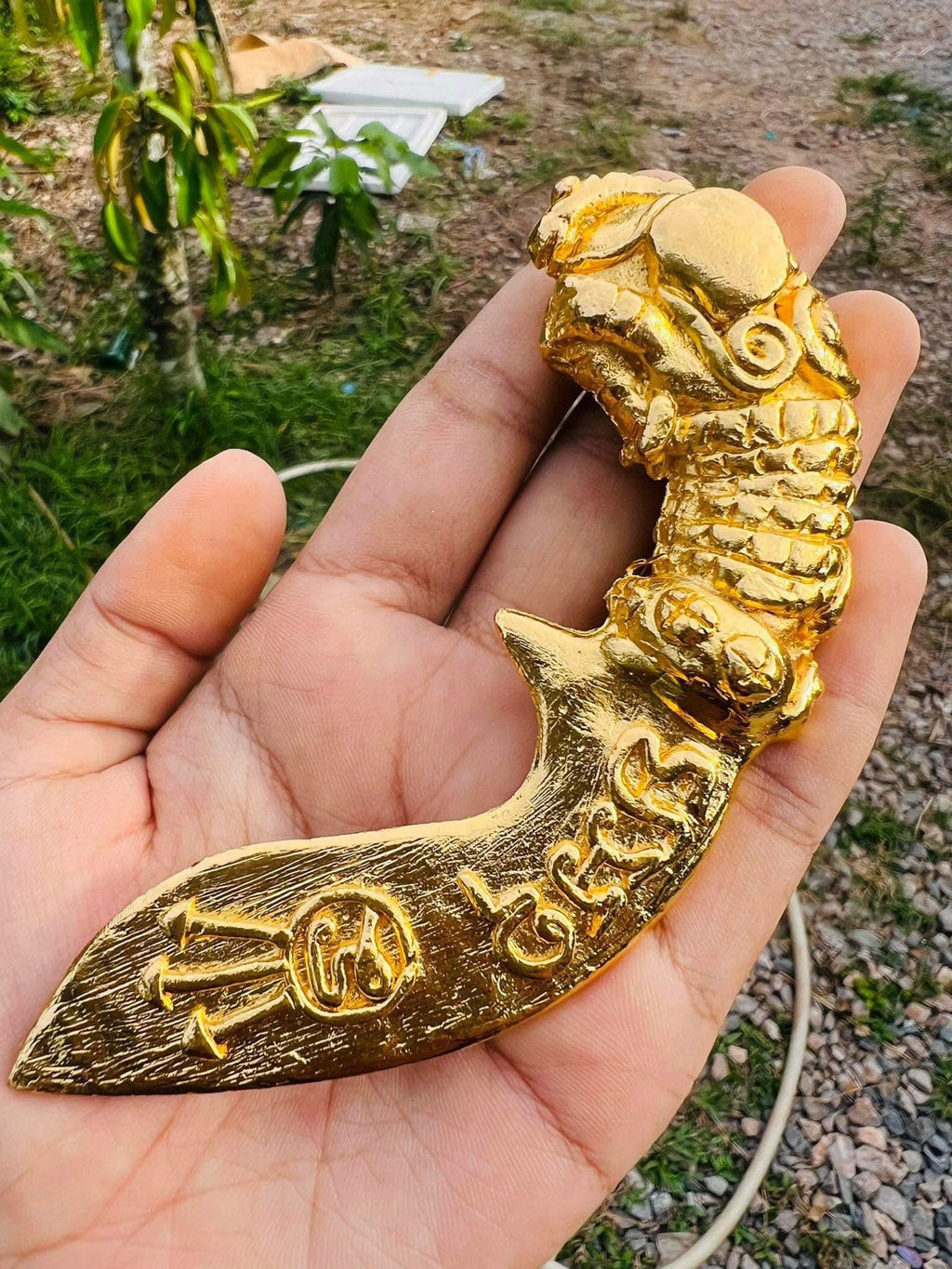 Hand holding gold tone Thai mitmor dagger for protection amulet with ornate carved blade and dragon handle