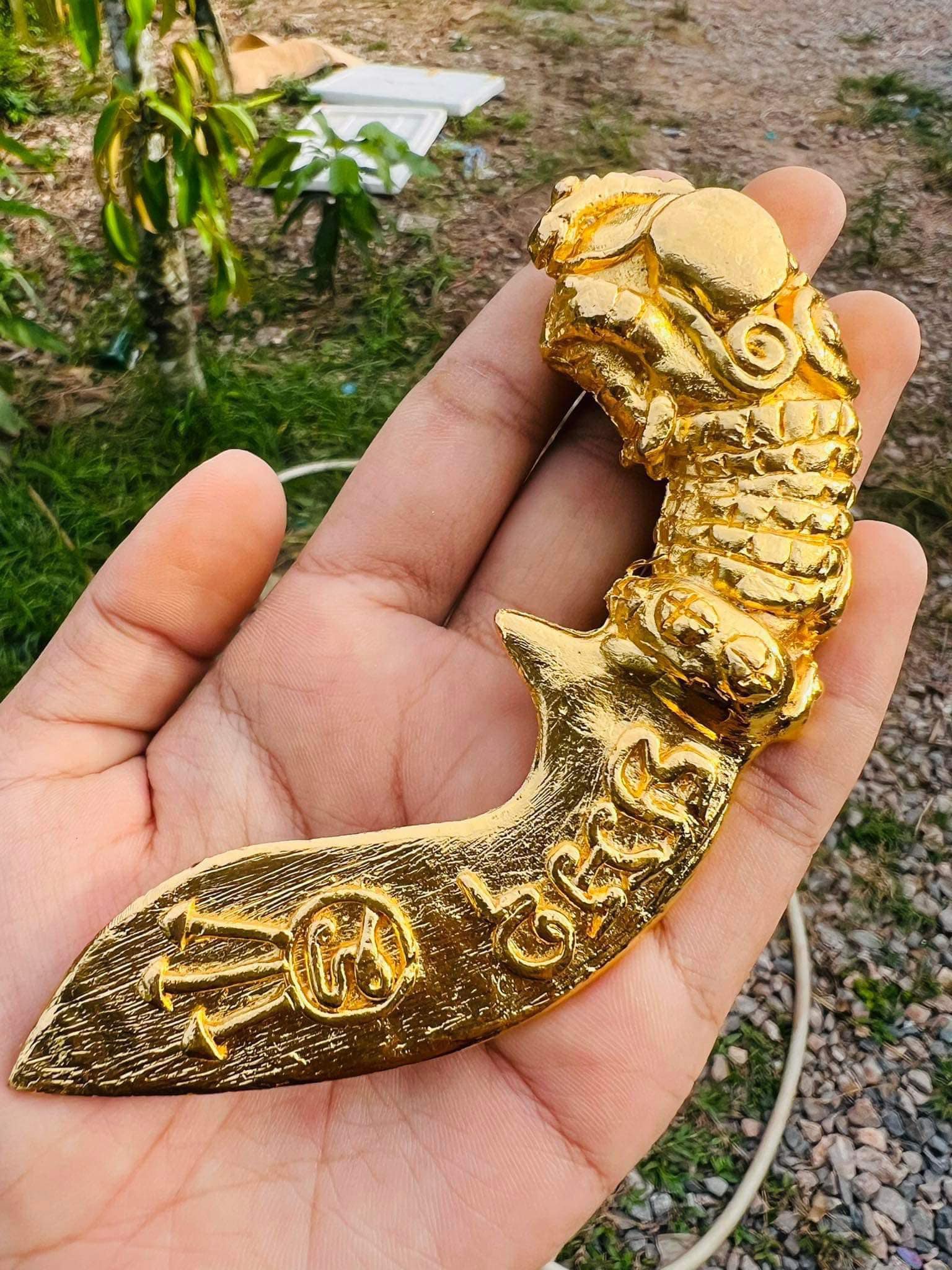 Hand holding gold tone Thai mitmor dagger for protection amulet with ornate carved blade and dragon handle