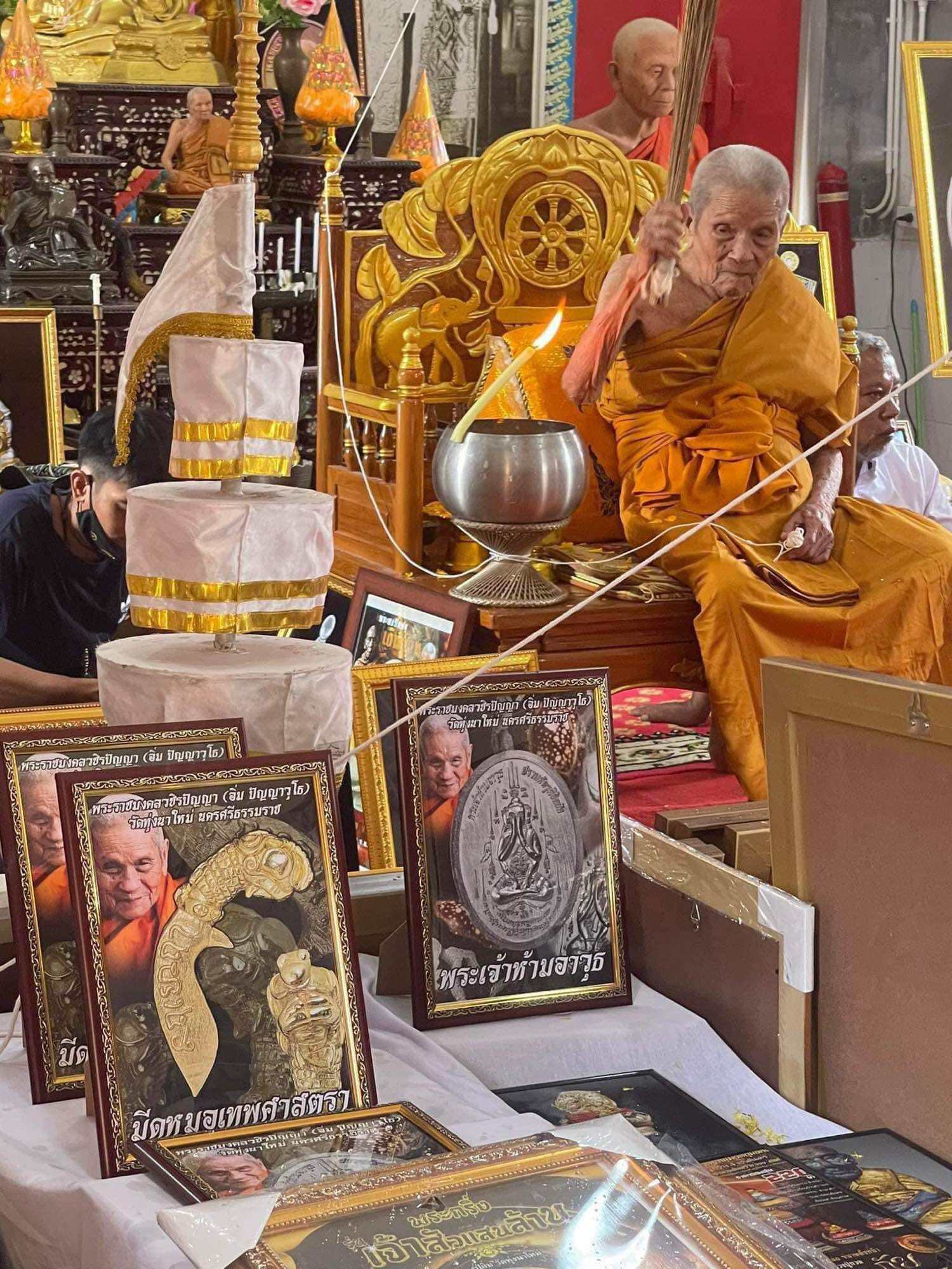 Thai mitmor dagger for protection amulets displayed with framed images and a Buddhist monk blessing ceremony