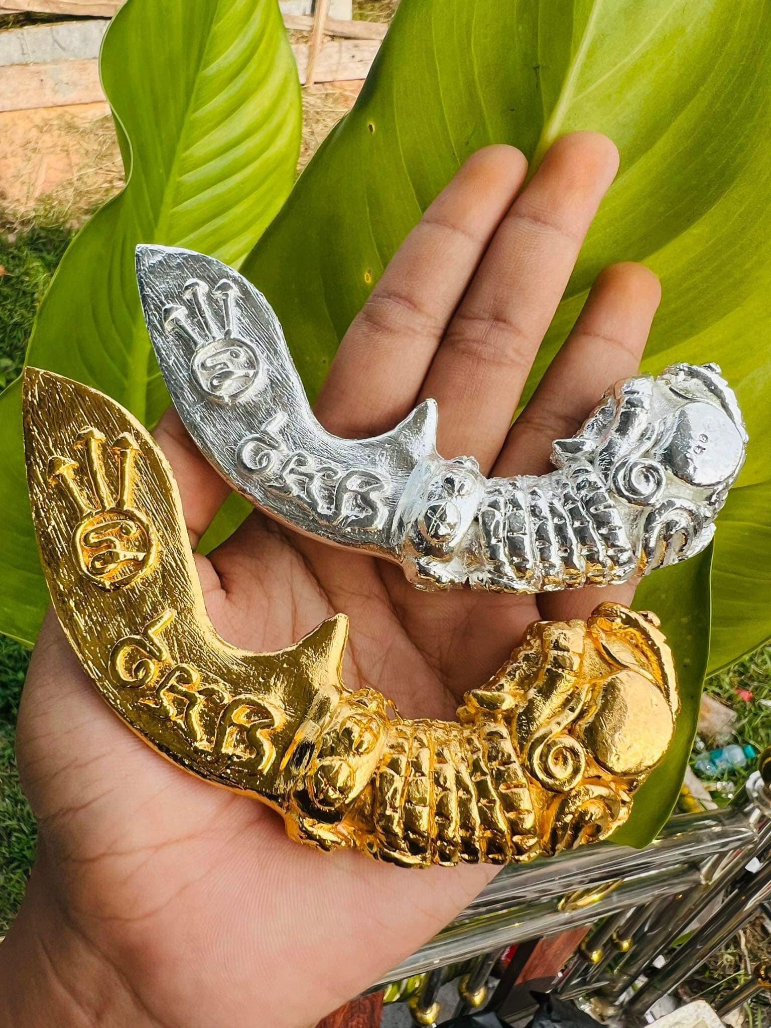 Hand holding gold and silver Thai mitmor dagger for protection amulets with ornate carved details by Thai Blessing Co