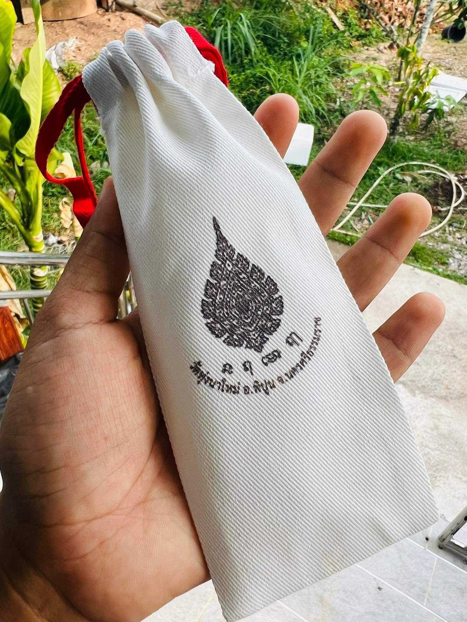 Thai mitmor dagger for protection in white drawstring pouch with red cord held in hand outside