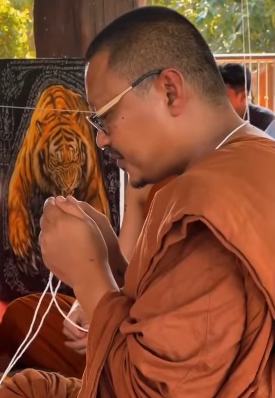 Thai monk blessing a pendant with white cord before tiger painting Thai tiger amulet for power and protection