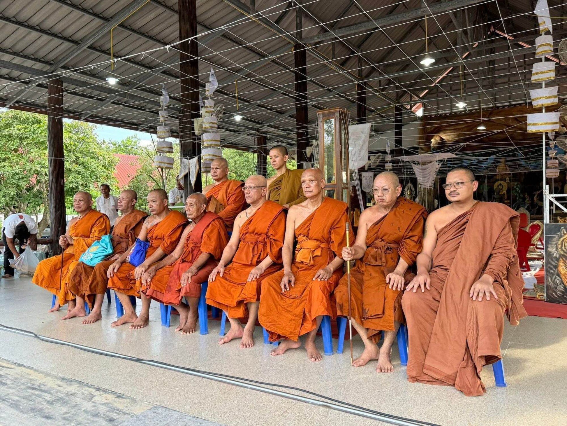 Group of Thai monks in orange robes seated during blessing ceremony for Thai tiger amulet for power and protection.