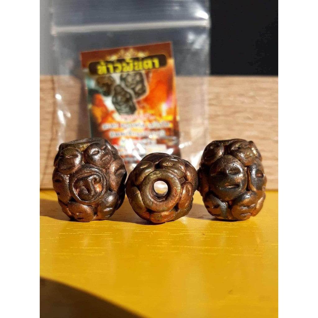 Three carved bronze beads on yellow surface with package in background Thao Phan Ta amulet for protection.