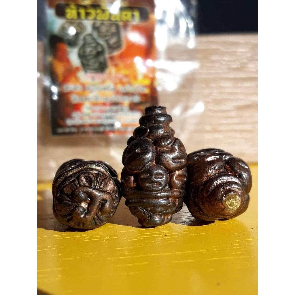 Thao Phan Ta amulet for protection. Three small carved dark talismans on yellow surface with blurred packaging