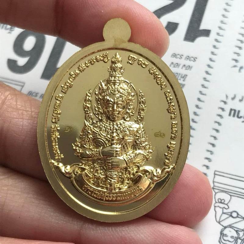 Thao Wessuwan amulet for wealth gold oval amulet held between fingers with embossed deity and Thai script