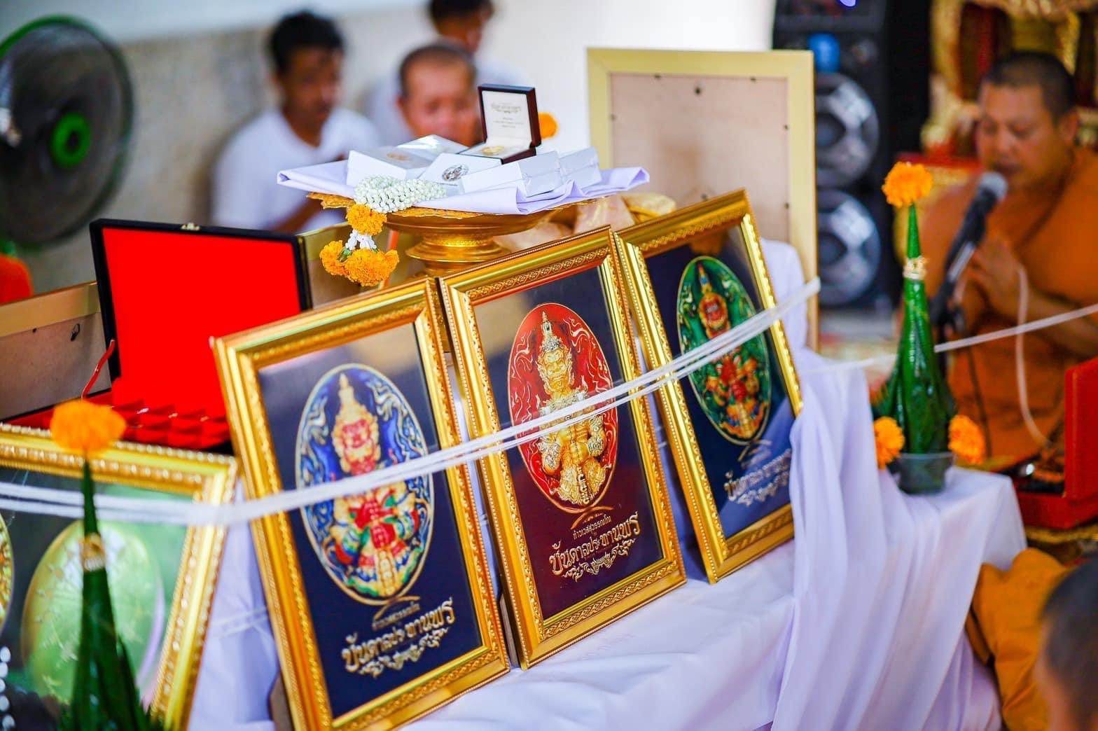 Three gold framed amulet plaques of Thao Wessuwanno Bandarn Patthanapon displayed on ceremonial offering table with monk
